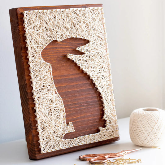 A charming rabbit string art sign made with white string on a dark wooden background, depicting a sitting rabbit silhouette.