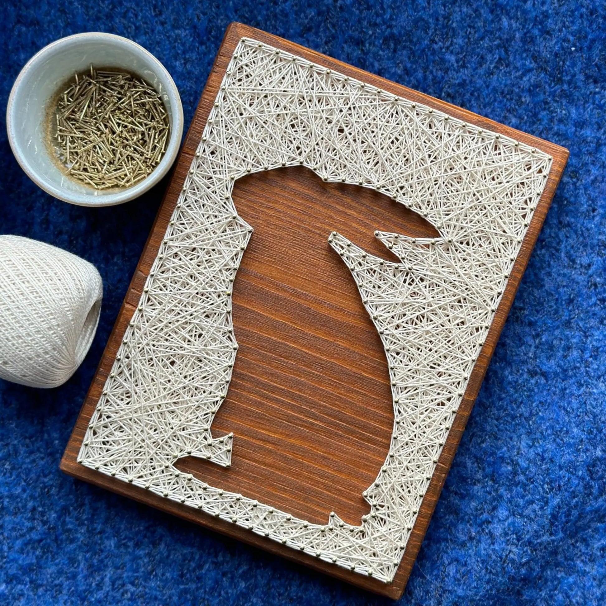 A charming rabbit string art sign made with white string on a dark wooden background, depicting a sitting rabbit silhouette.