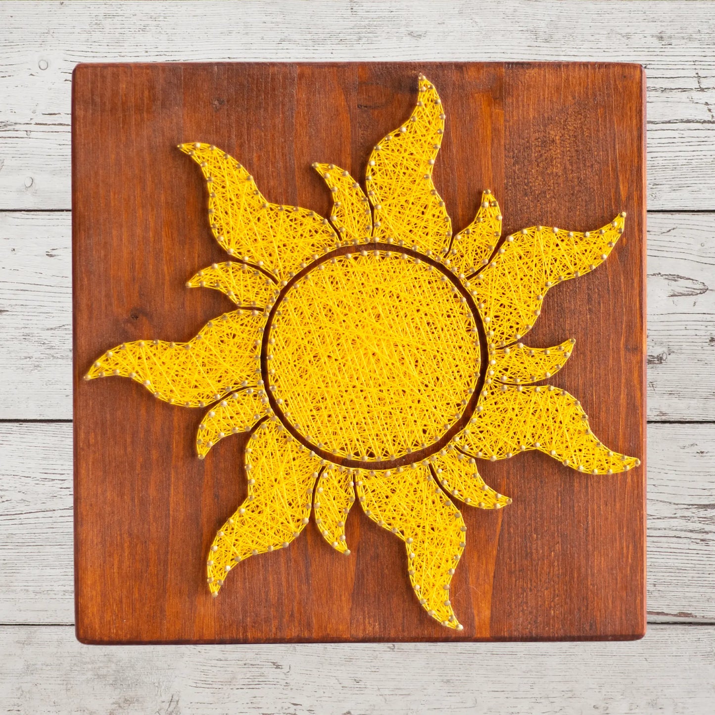 A vibrant sun string art sign made with yellow string on a dark wooden background, showcasing a bright and cheerful sun design.