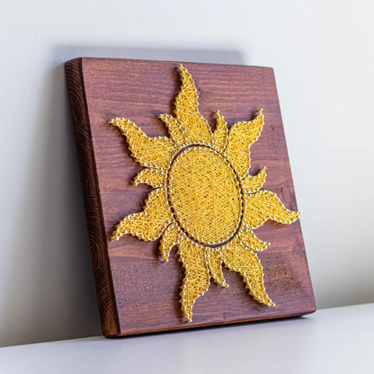 A vibrant sun string art sign made with yellow string on a dark wooden background, showcasing a bright and cheerful sun design.