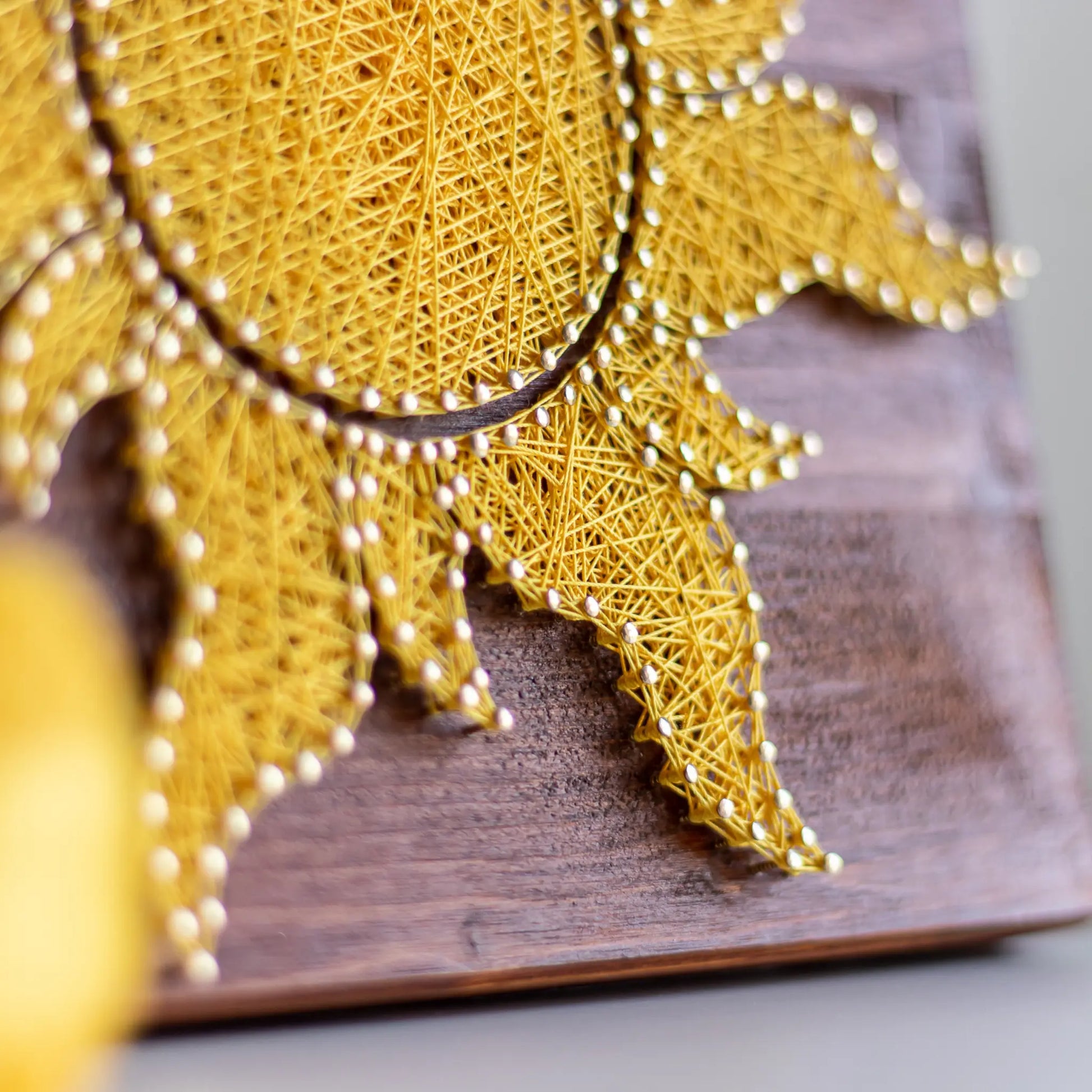 A vibrant sun string art sign made with yellow string on a dark wooden background, showcasing a bright and cheerful sun design.