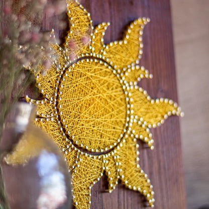 A vibrant sun string art sign made with yellow string on a dark wooden background, showcasing a bright and cheerful sun design.