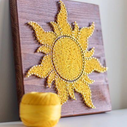 A vibrant sun string art sign made with yellow string on a dark wooden background, showcasing a bright and cheerful sun design.