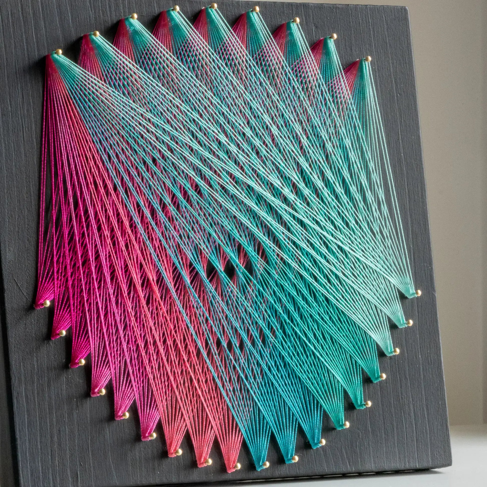 Geometric string art with pink and teal threads on black base, part of craft kits for adults, highlighting intricate design.DIY geometric string art kit featuring a vibrant mandala design with multiple color options on a black wooden board by GoodStrings - pink and teal