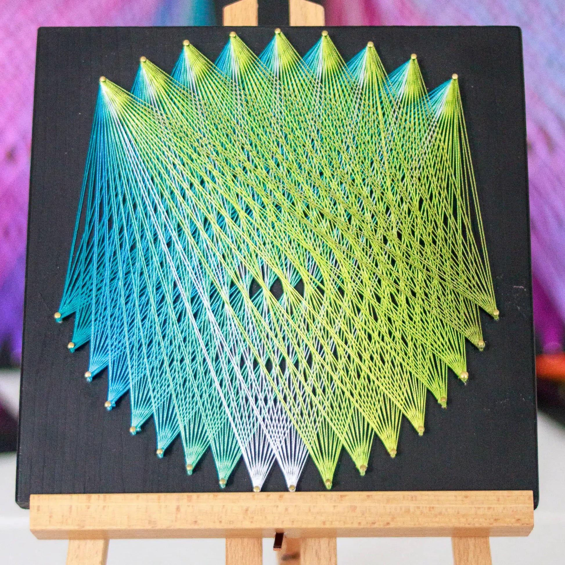 Geometric string art with blue and green threads on black base, perfect craft kit for adults, showcasing detailed pattern on easel - green and blue