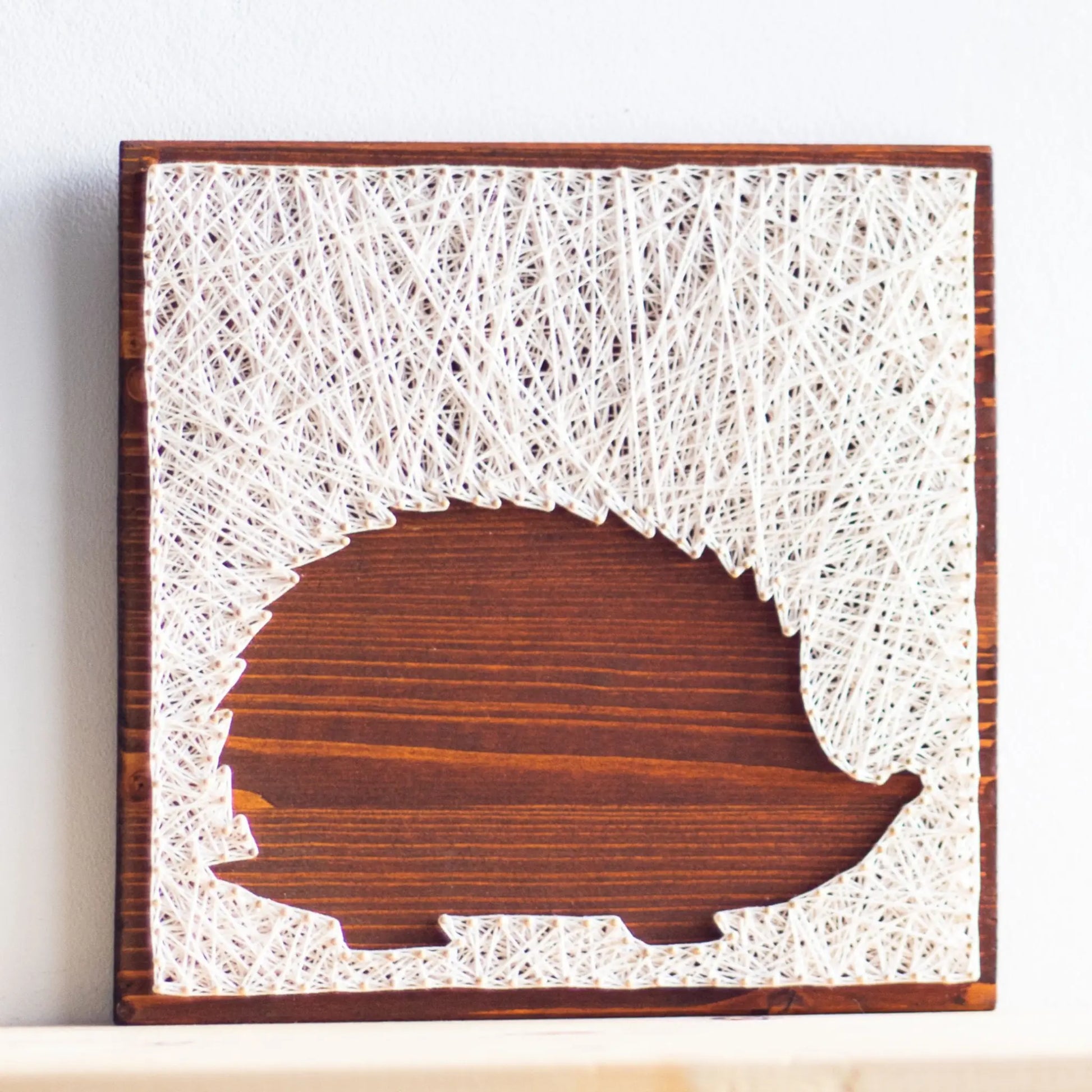 DIY string art kit featuring a hedgehog silhouette outlined with ivory thread on a rustic wooden board by GoodStrings - front view