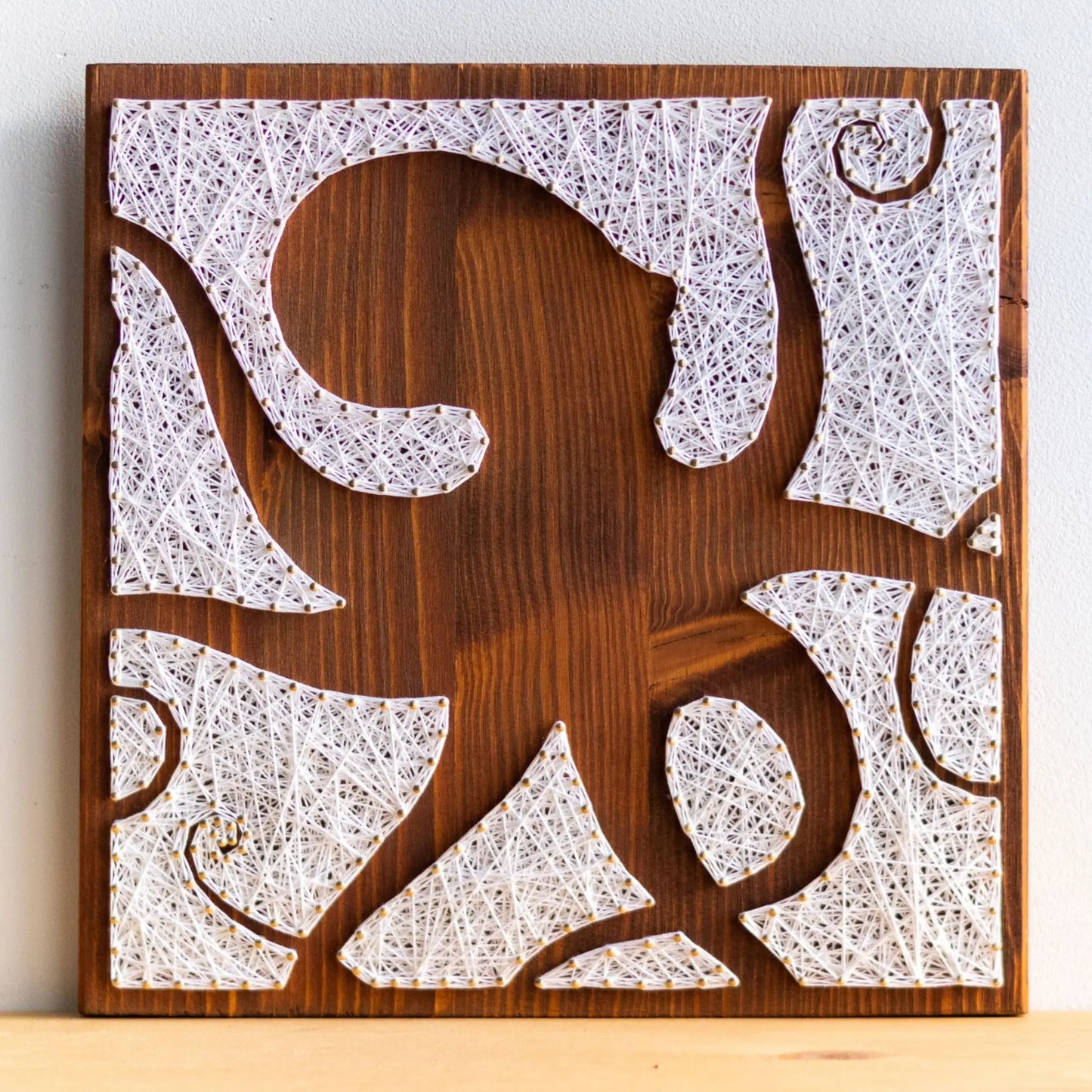 DIY string art kit featuring an octopus silhouette with various geometric shapes created with white threads on a dark wooden board by GoodStrings