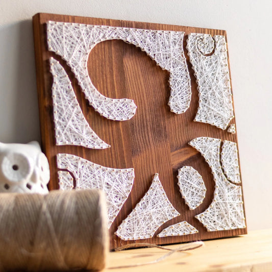 DIY string art kit featuring an octopus silhouette with various geometric shapes created with white threads on a dark wooden board by GoodStrings