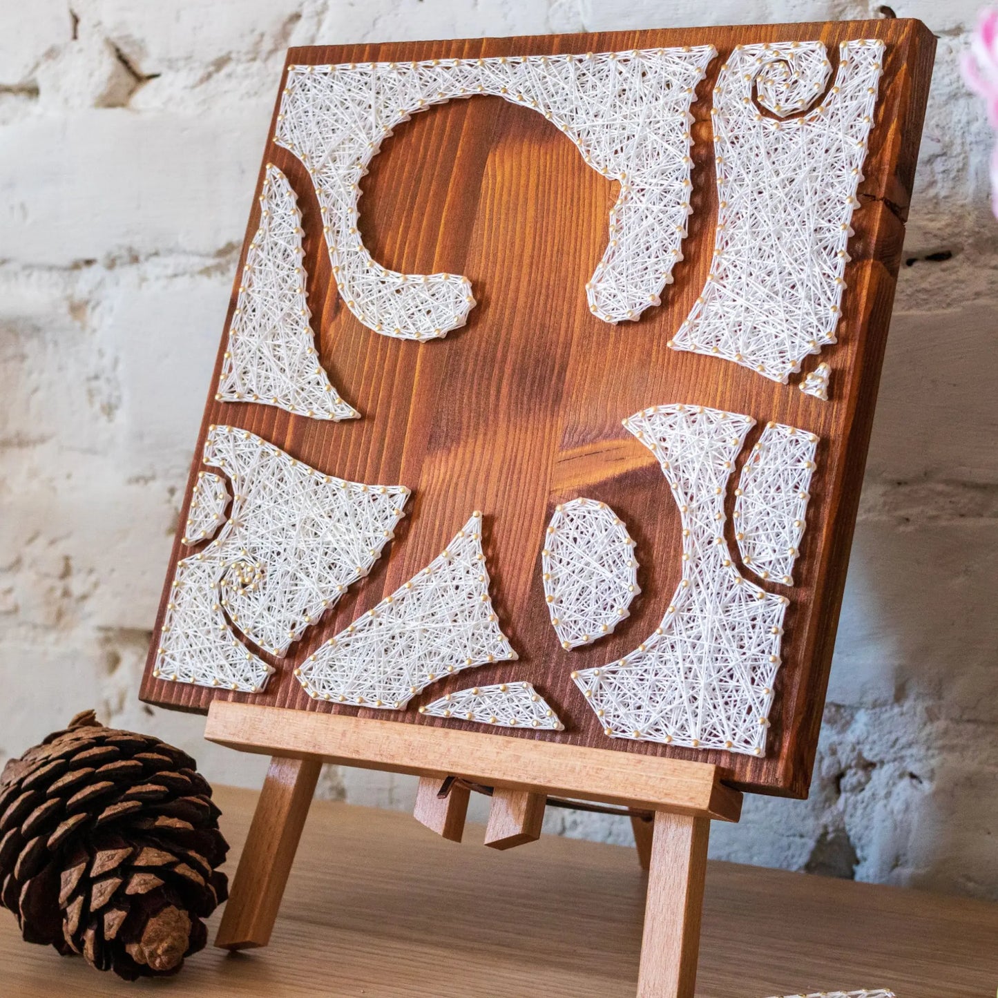 DIY string art kit featuring an octopus silhouette with various geometric shapes created with white threads on a dark wooden board by GoodStrings