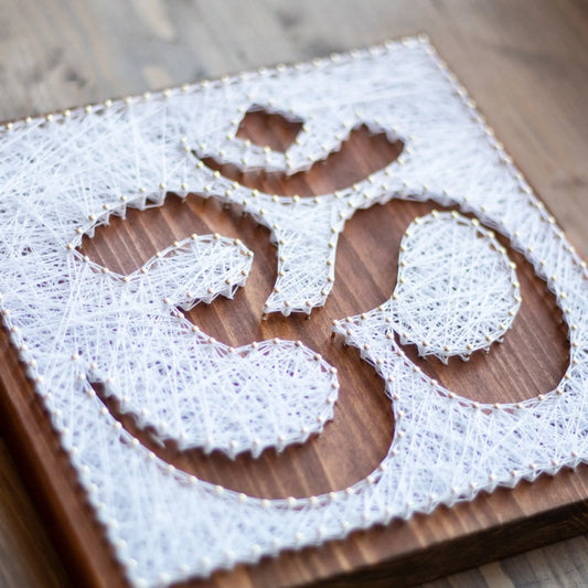 DIY string art kit featuring an Om symbol outlined with white thread on a rustic wooden board by GoodStrings - top view