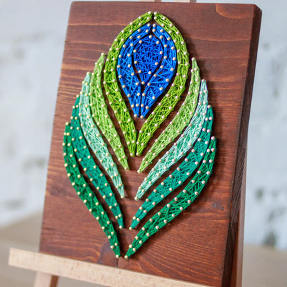 DIY string art kit featuring a peacock feather design with vibrant blue, green, and lime threads on a rustic wooden board by GoodStrings - right side view