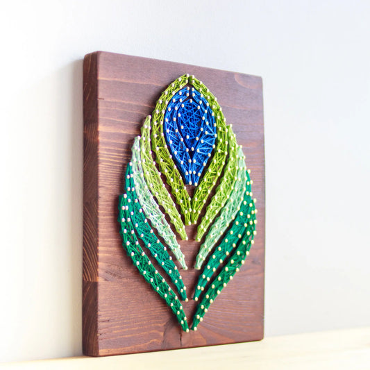 DIY string art kit featuring a peacock feather design with vibrant blue, green, and lime threads on a rustic wooden board by GoodStrings - side view