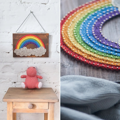 DIY string art kit featuring a vibrant rainbow arching over fluffy clouds, crafted with colorful threads on a dark wooden board, designed by GoodStrings