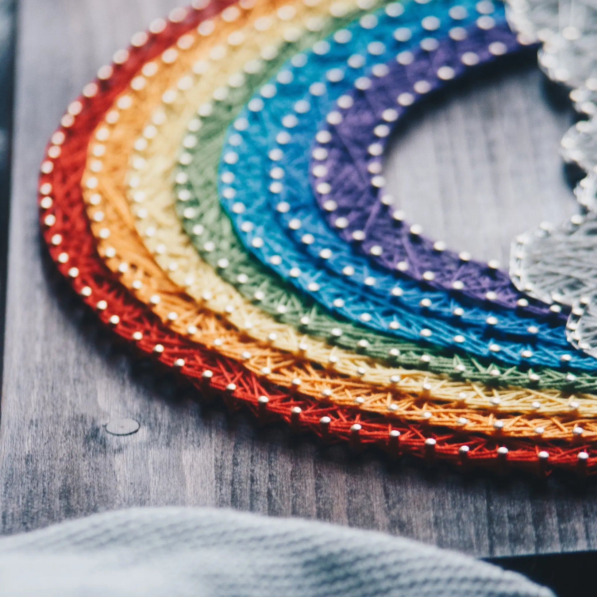 DIY string art kit featuring a vibrant rainbow arching over fluffy clouds, crafted with colorful threads on a dark wooden board, designed by GoodStrings