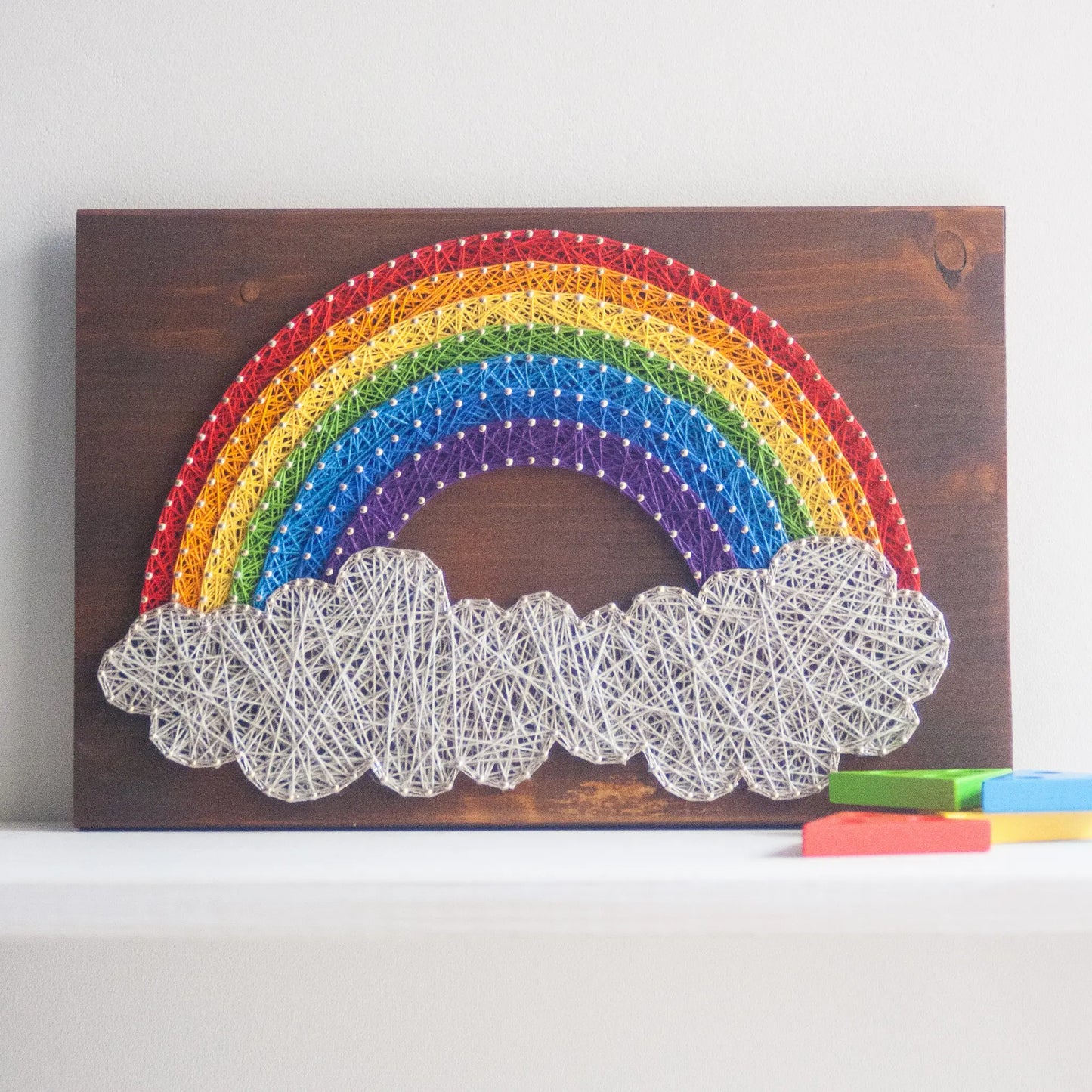 DIY string art kit featuring a vibrant rainbow arching over fluffy cloud, crafted with colorful threads on a dark wooden board, designed by GoodStrings