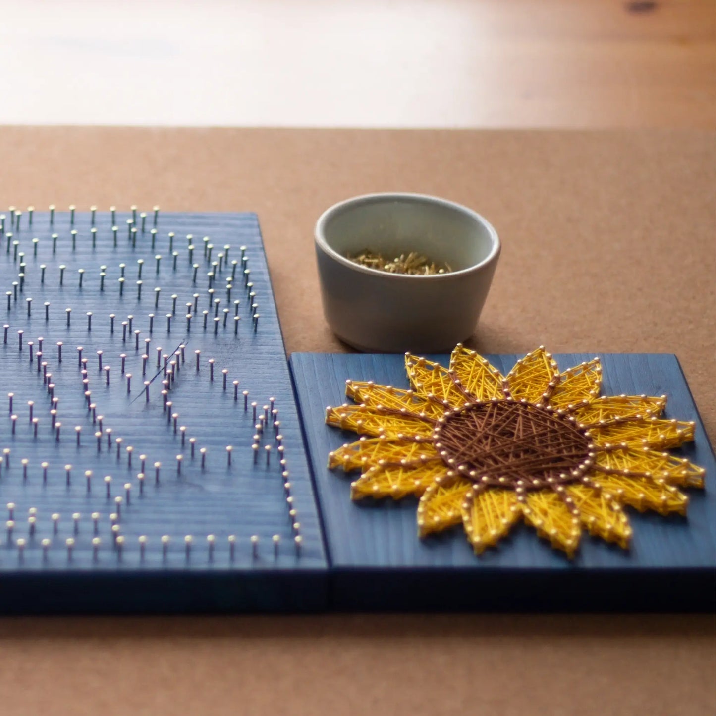 DIY string art kit featuring a bright yellow sunflower with a brown center created with threads on a dark blue wooden board by GoodStrings