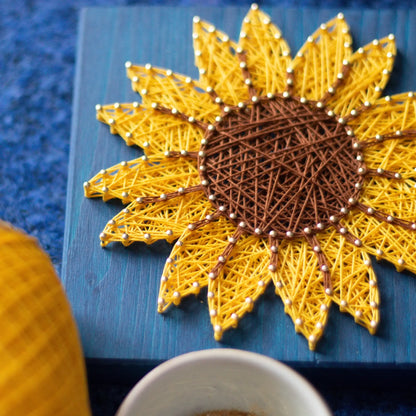 DIY string art kit featuring a bright yellow sunflower with a brown center created with threads on a dark blue wooden board by GoodStrings