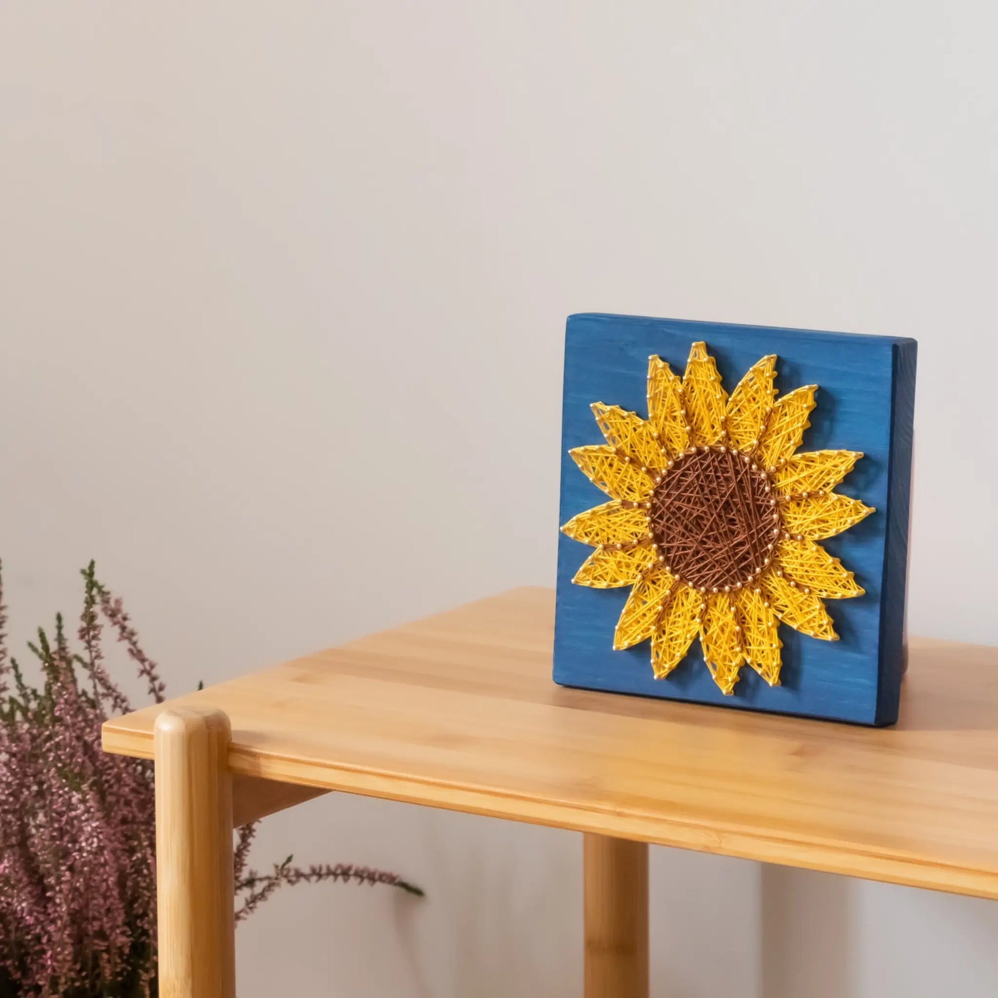 DIY string art kit featuring a bright yellow sunflower with a brown center created with threads on a dark blue wooden board by GoodStrings