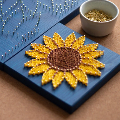 DIY string art kit featuring a bright yellow sunflower with a brown center created with threads on a dark blue wooden board by GoodStrings