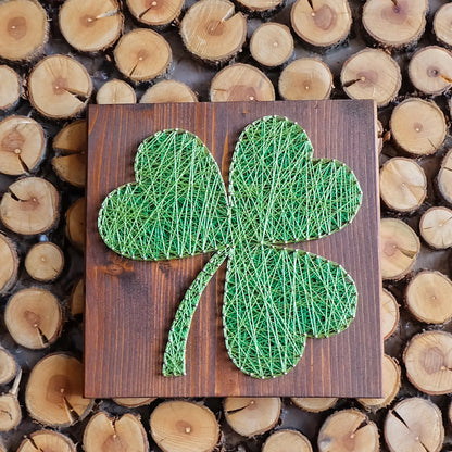 DIY string art kit featuring a three-leaf clover outlined with green thread on a rustic wooden board by GoodStrings - top view, brown background