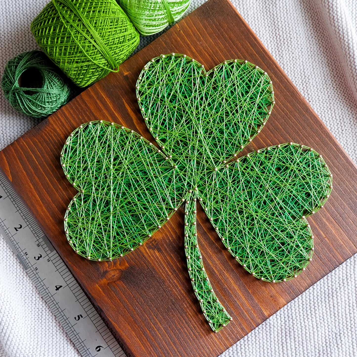 DIY string art kit featuring a three-leaf clover outlined with green thread on a rustic wooden board by GoodStrings - TOP VIEW