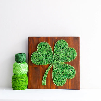 DIY string art kit featuring a three-leaf clover outlined with green thread on a rustic wooden board by GoodStrings - front view on a white background