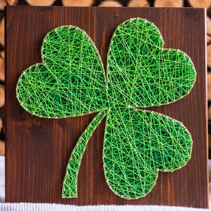 DIY string art kit featuring a three-leaf clover outlined with green thread on a rustic wooden board by GoodStrings - zoomed it front view