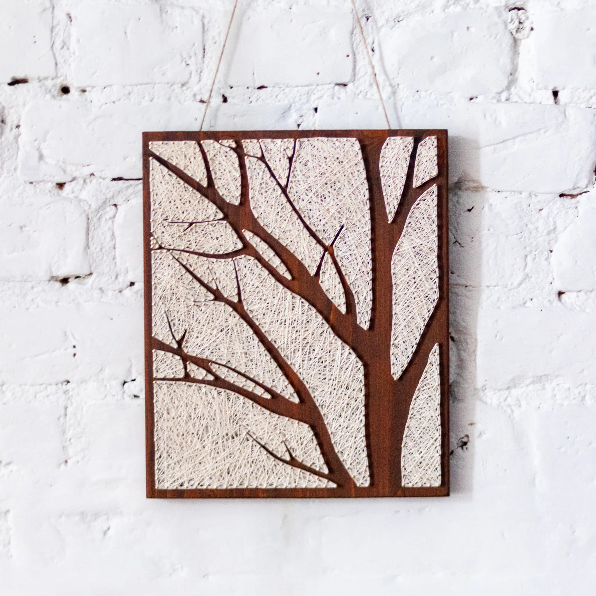 DIY string art craft kit for adults featuring a tree silhouette design, displayed on a natural wooden board with ivory thread.