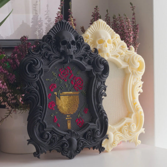 Gothic cross stitch frames in black and ivory with ornate skull design, one stitched with floral chalice pattern and one blank frame on display