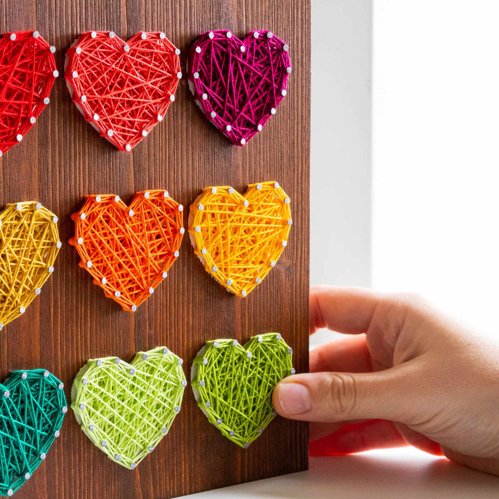 Close up. Heart string art pattern design on a wooden board featuring multiple heart shapes. A DIY craft project, perfect for home decor, made using nails and string. Available as a digital download for easy crafting.