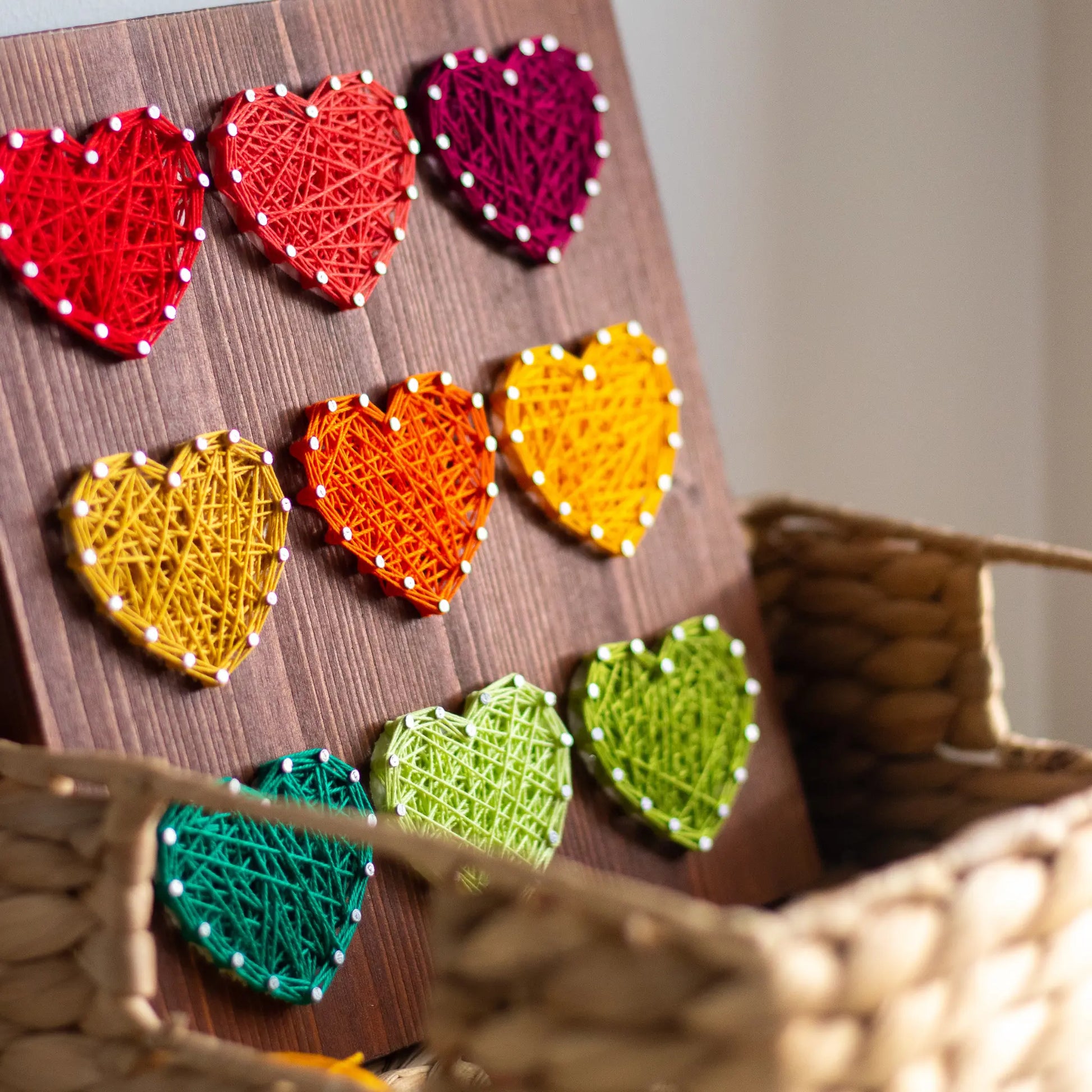 Colorful hearts string art pattern arranged neatly in a basket, showing vibrant handcrafted hearts on a wooden board.