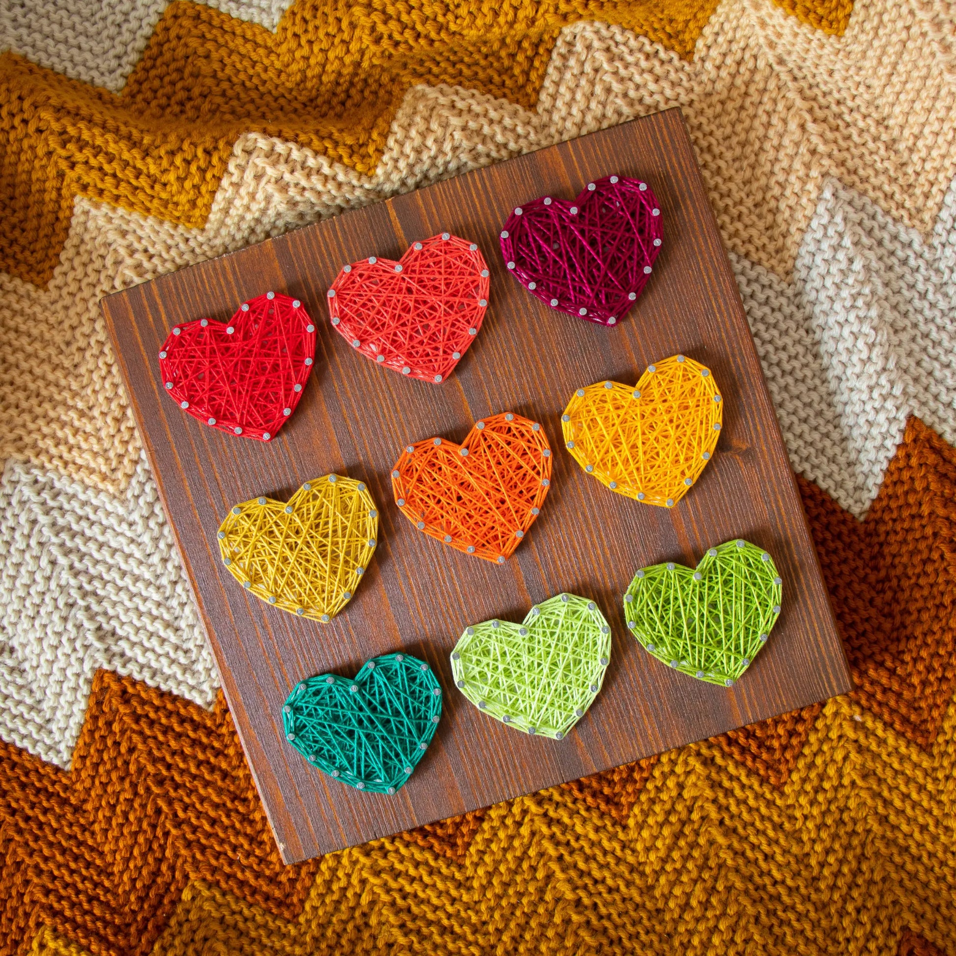 Heart string art pattern design on a Top view. Wooden board featuring multiple heart shapes. A DIY craft project, perfect for home decor, made using nails and string. Available as a digital download for easy crafting.