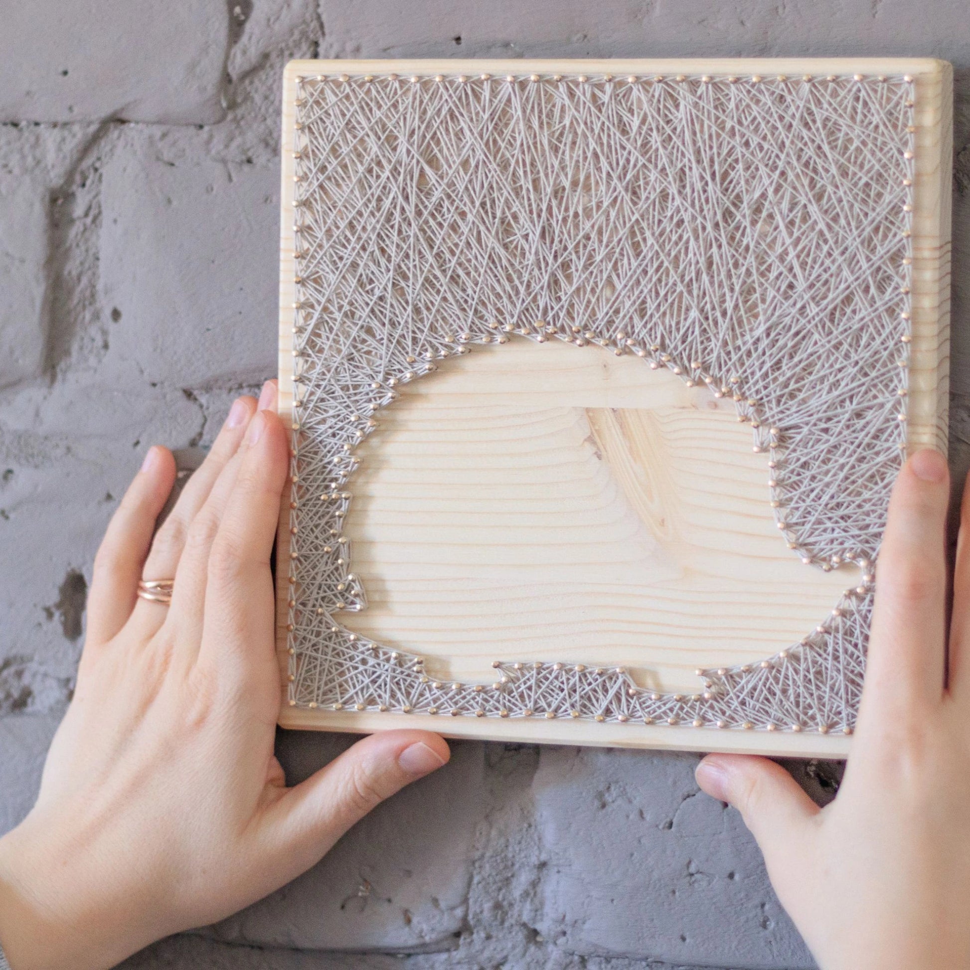 Hands holding hedgehog silhouette string art pattern on a light wooden base with ivory thread, designed for beginners. Available as a digital download for easy, DIY home decor.