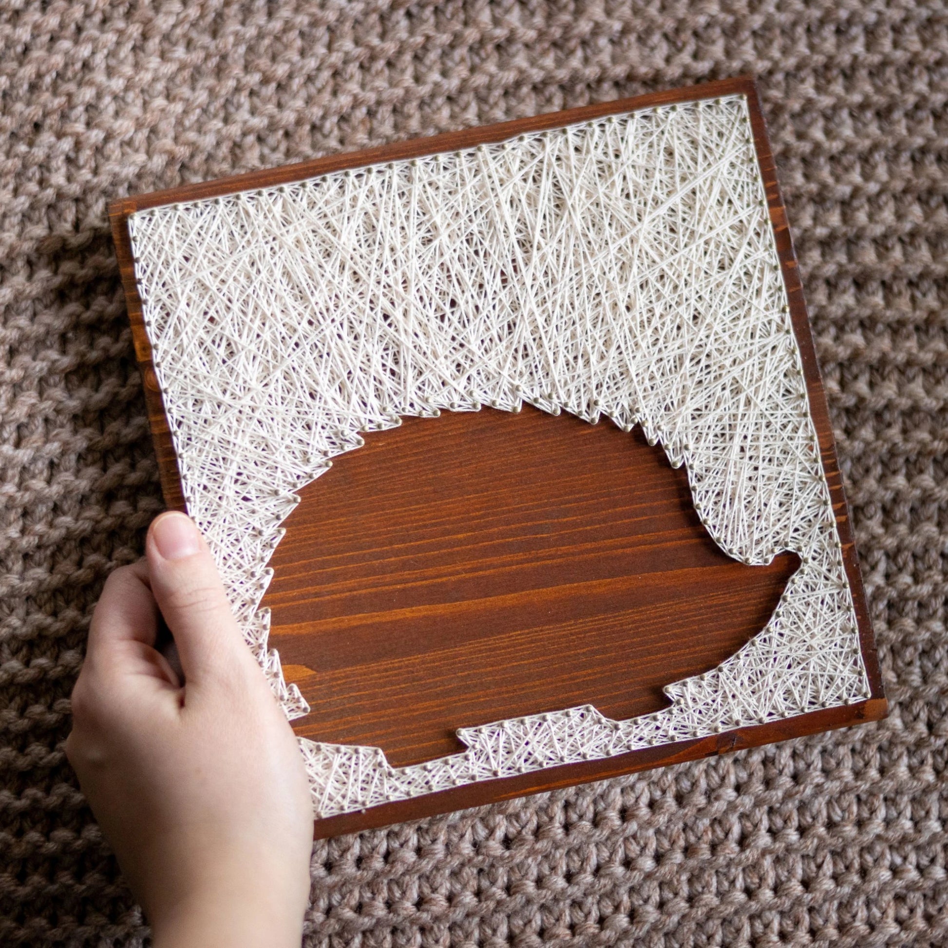 Hand holding hedgehog silhouette string art pattern on a wooden base with ivory thread, designed for beginners. Available as a digital download for easy, DIY home decor.