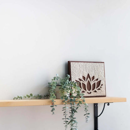 lotus string art sign on a brown wood base on a shelf