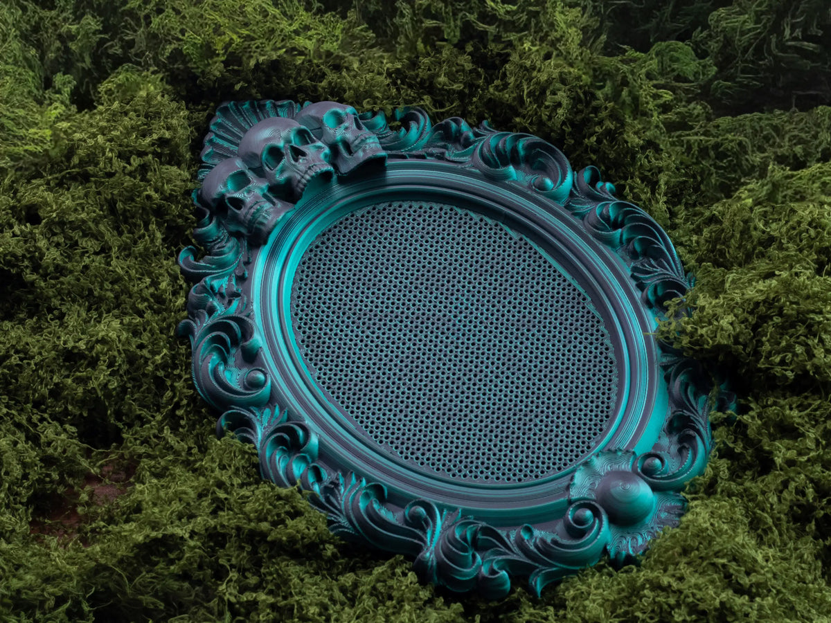 Gothic oval cross stitch frame in Nightshade green with skull detail, shown from above on moss.