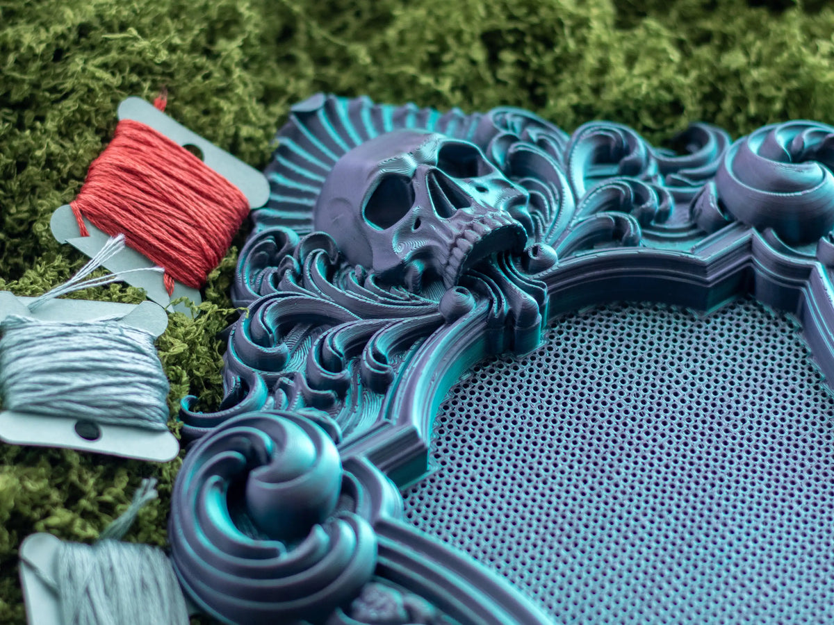 Close-up of a gothic cross stitch frame in Nightshade with embroidery floss, showing the perforated grid.