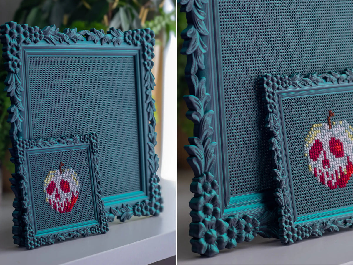 Gothic 3D printed cross stitch frame in Nightshade holding a finished poison-apple design, with a larger blank frame behind.