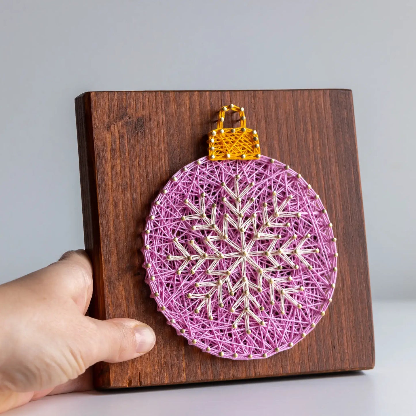 Handmade string art ornament on a wooden board held by a hand against a plain background