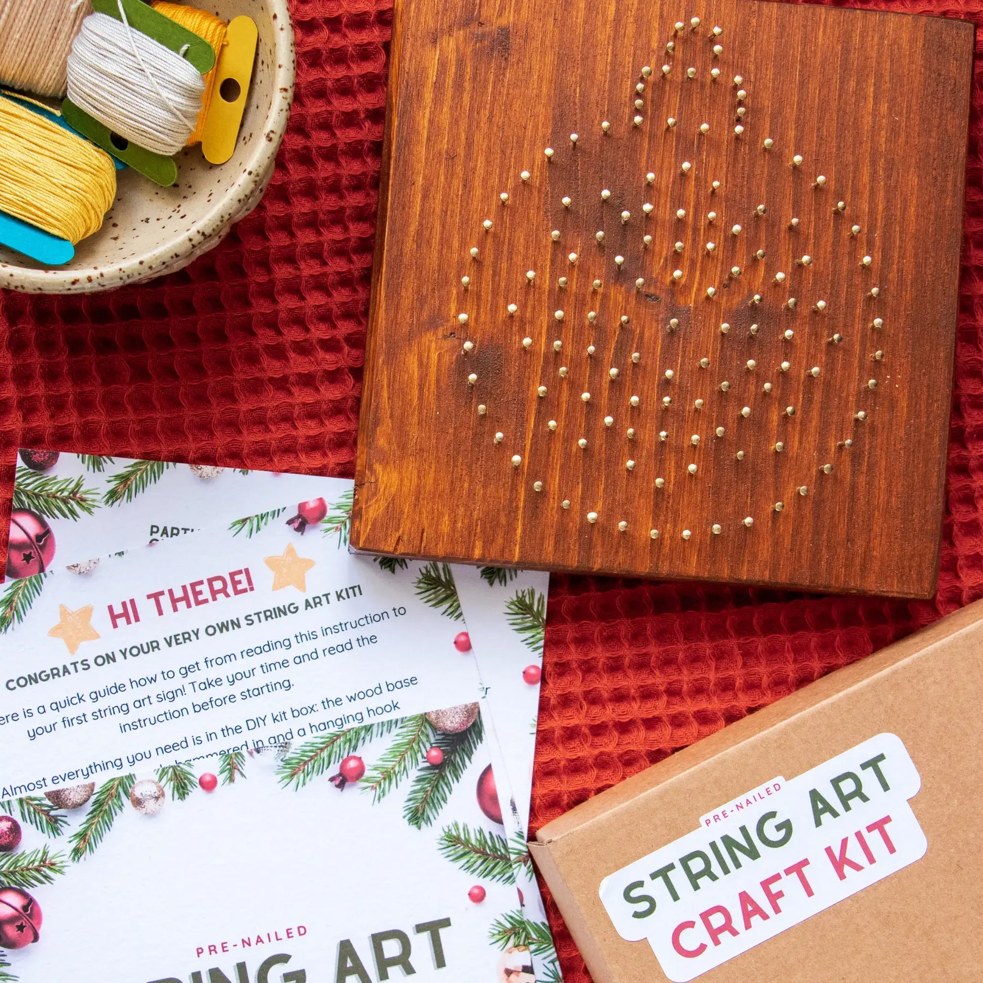 String art craft kit with wooden board, nails, and instructions on a red surface