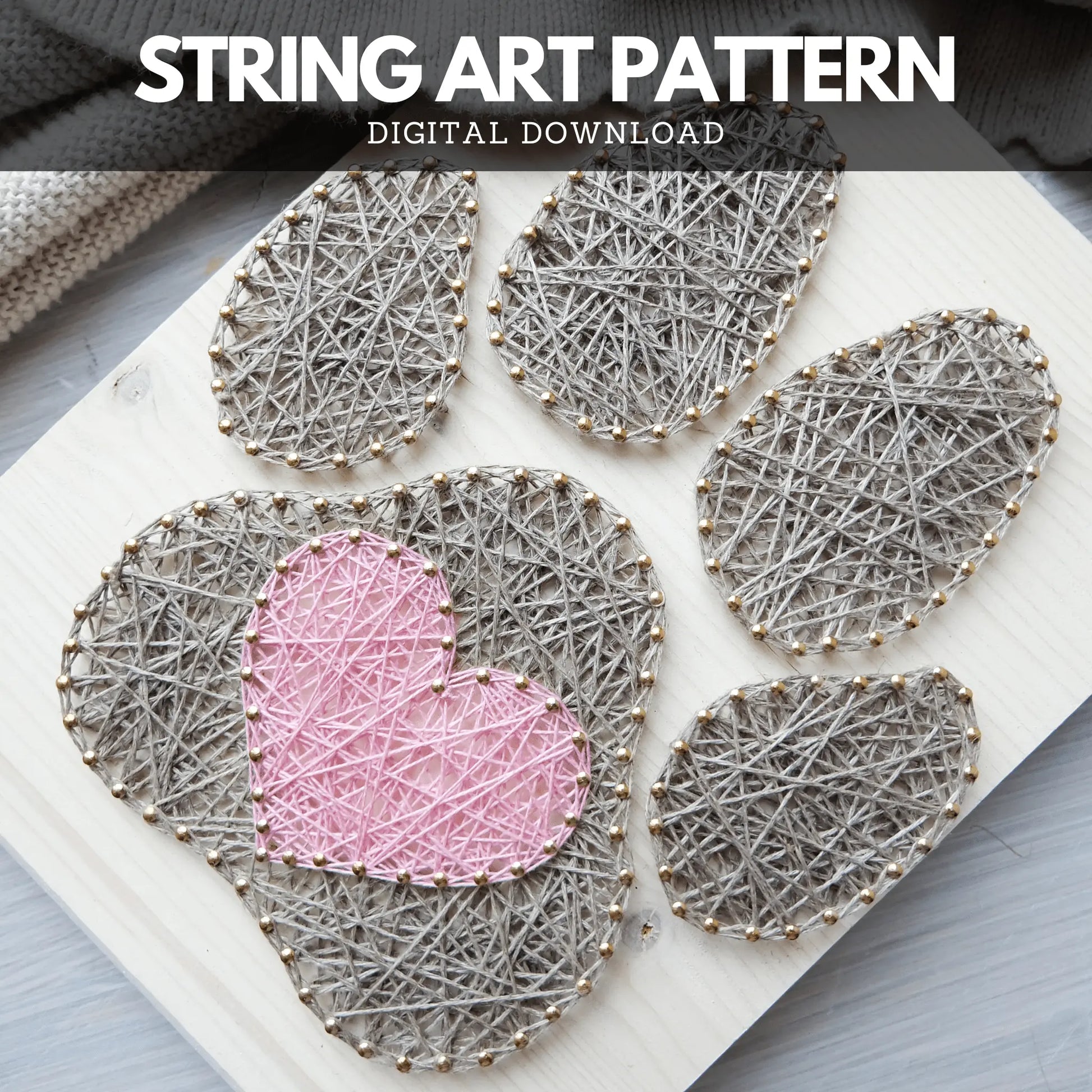 Dog paw string art pattern featuring a pink heart in the center of a grey paw print, crafted with detailed threading on a light wooden board.