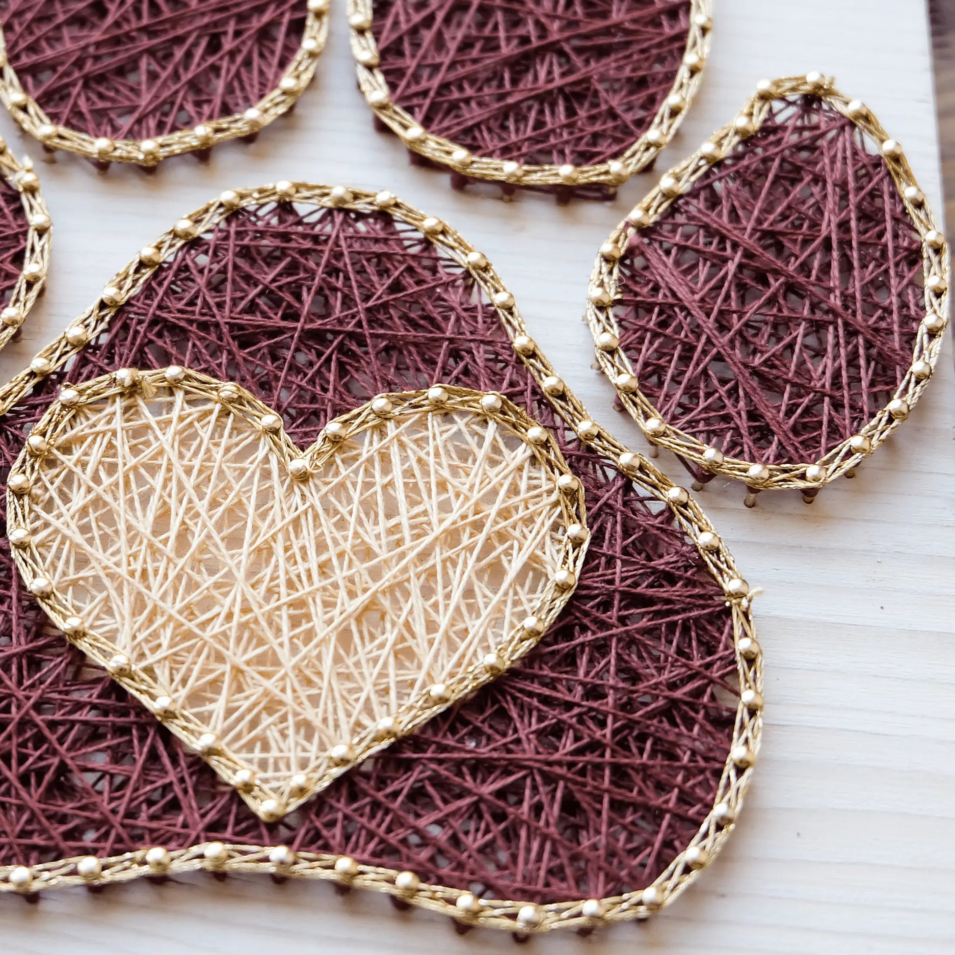 Detailed view of a dog paw string art pattern featuring a golden heart surrounded by burgundy threadwork, displayed on a wooden base.