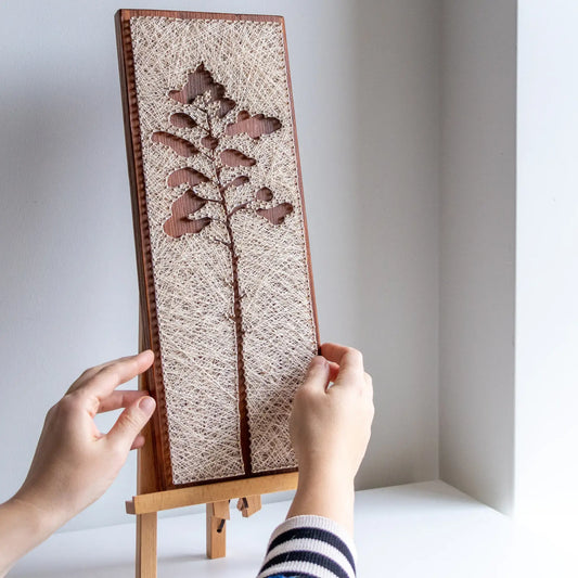 hand holding - Minimalist pine tree silhouette string art sign, handmade with simple lines and natural textures.