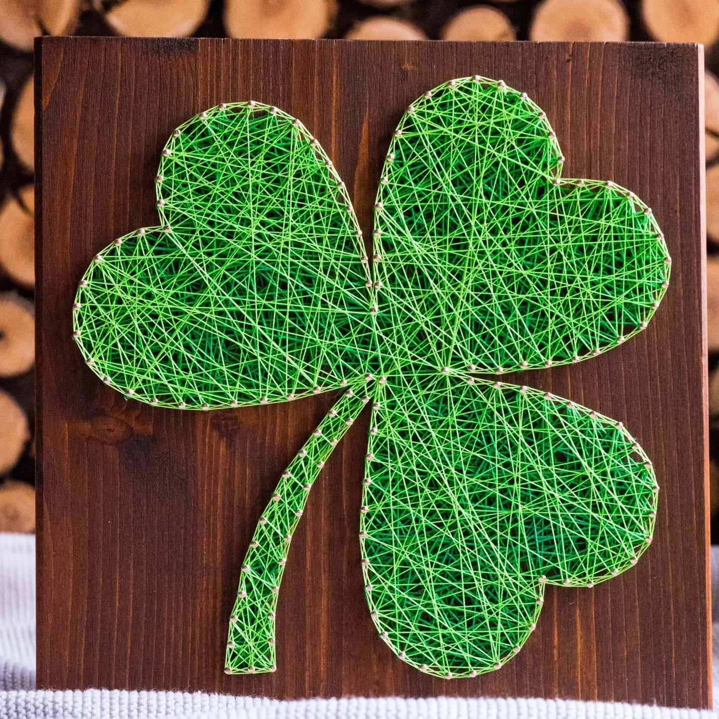 Shamrock string art pattern displayed on a wooden board, with green yarn spools beside it. Available as a digital download for creative DIY projects.