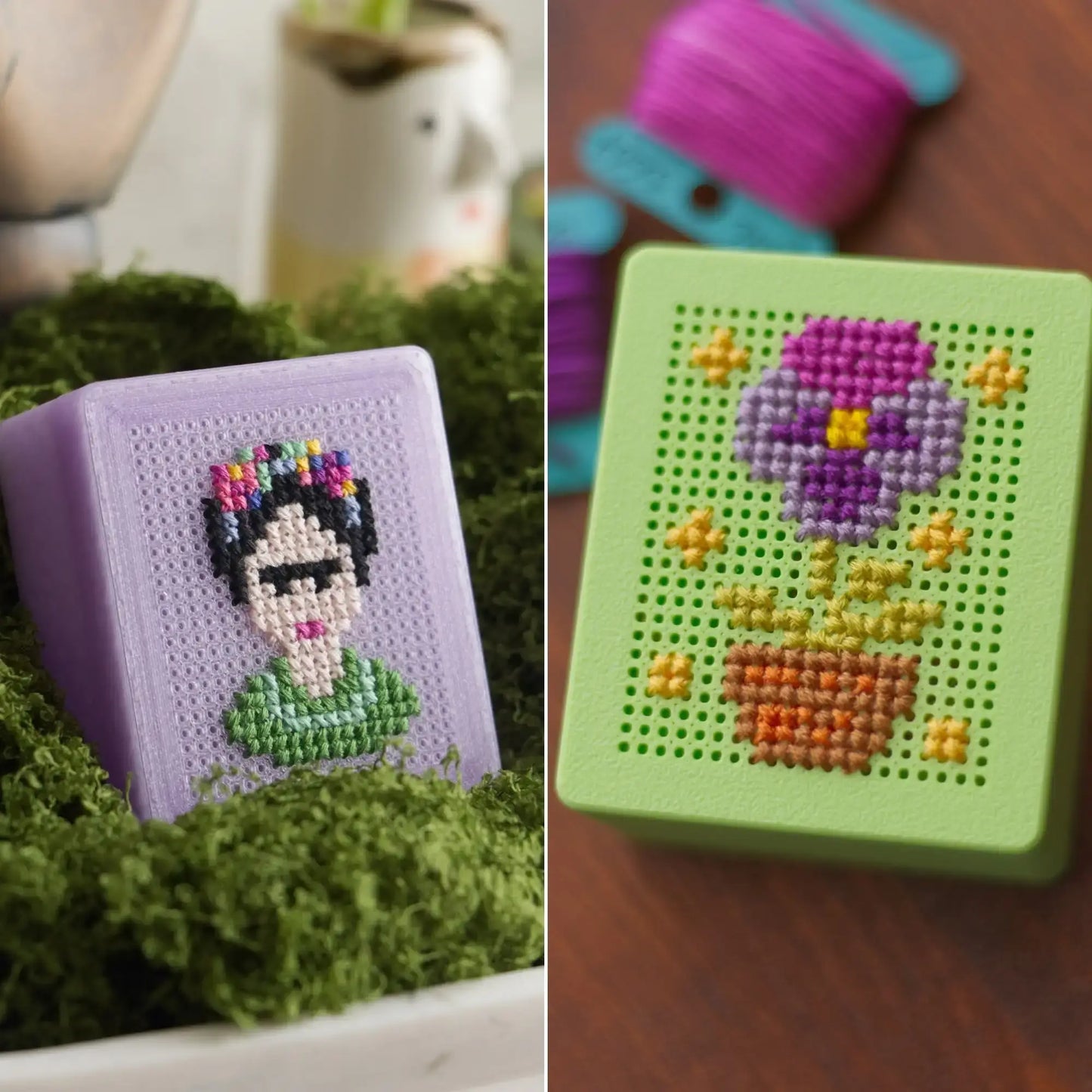 Two finished 3D-printed cross stitch boxes side by side: a lavender box with a Frida-inspired portrait design nestled in green moss, and a light green box with a purple flower and pot design on a wood surface.