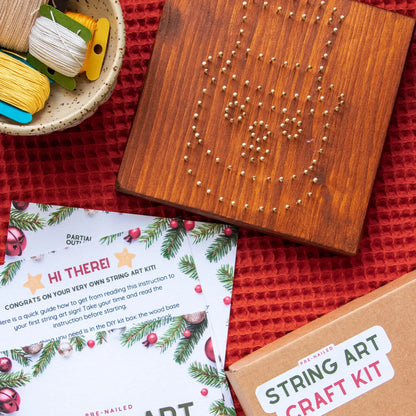 String art craft kit with wooden board, string, and instructions on a red textured surface