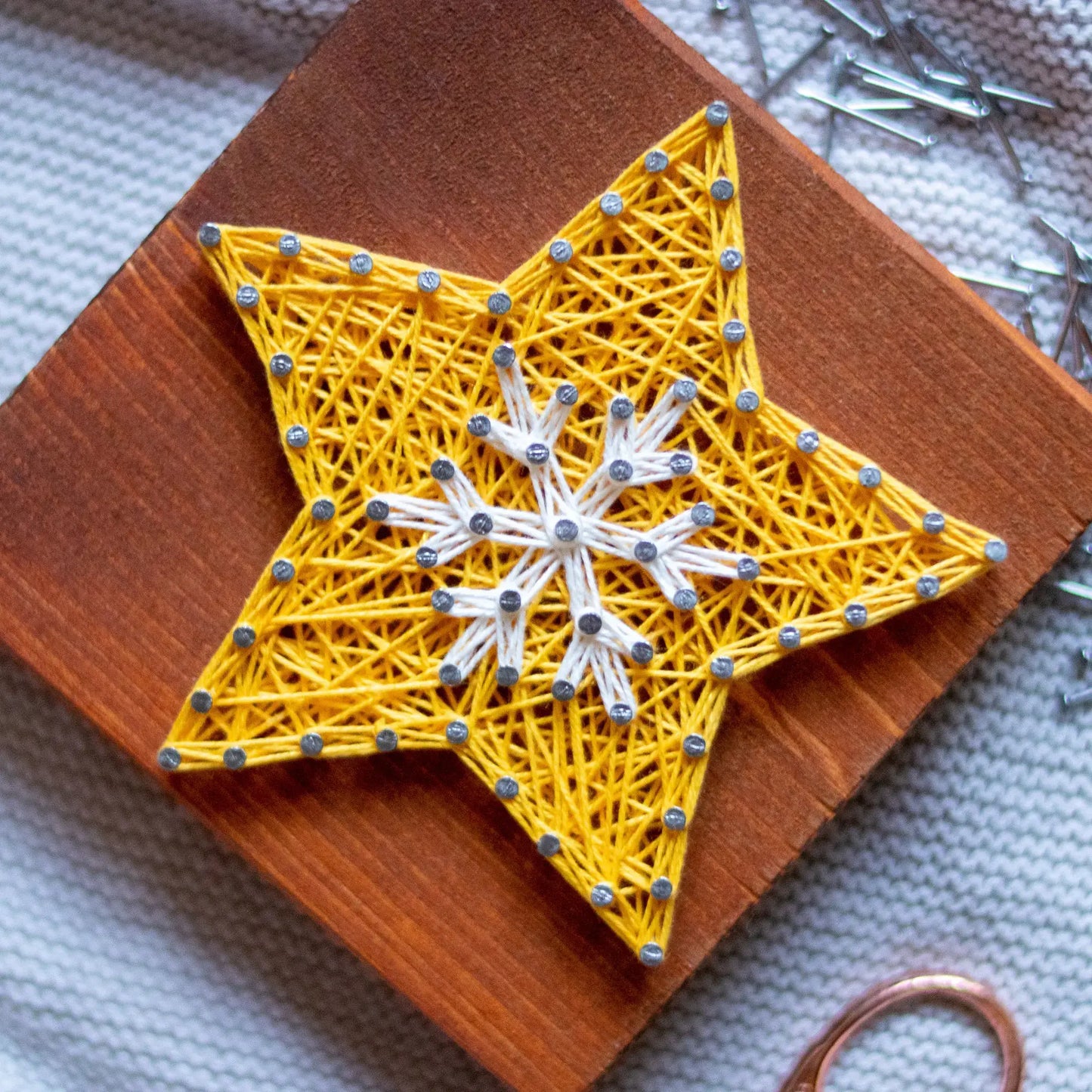 Finished yellow star with string art and white snowflake design on a wooden base