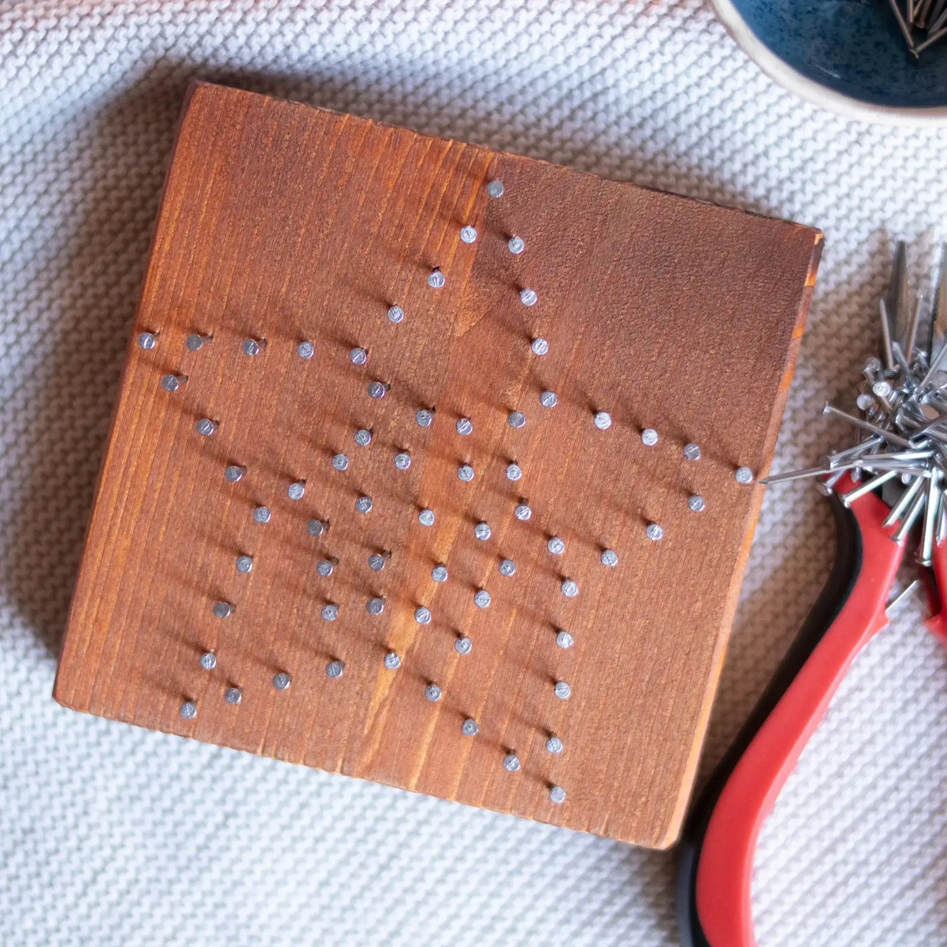 Wooden board with nails forming a star shape for string art project