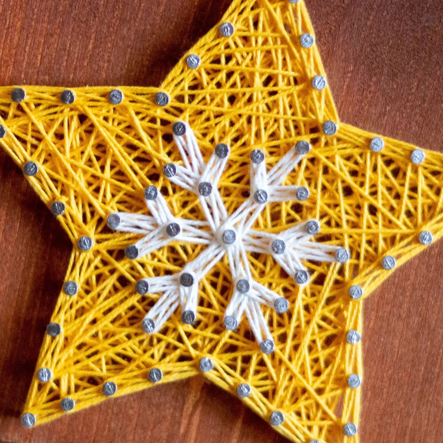 Close-up of yellow star string art with white snowflake details on a wooden base