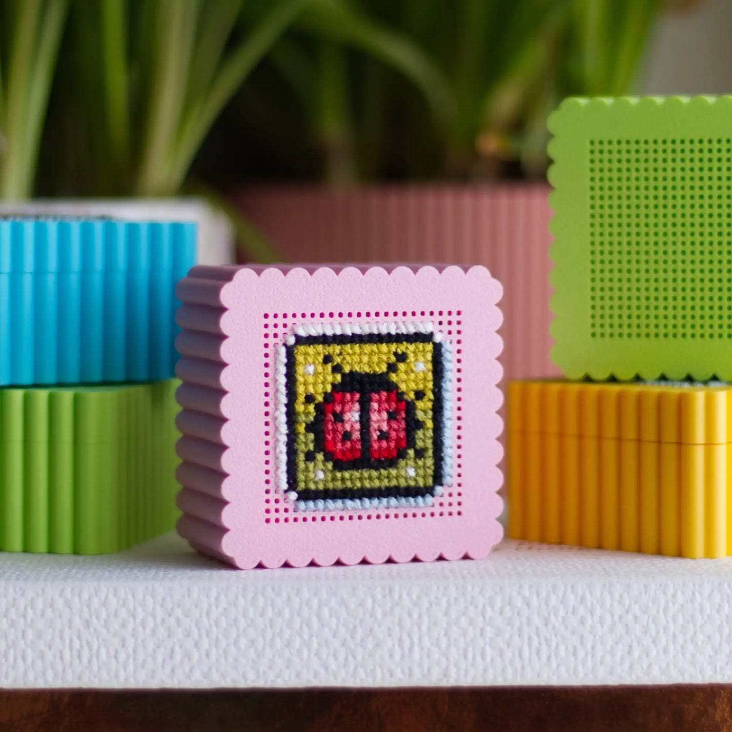 Mini cross stitch boxes in pastel colors with perforated lids, pink box showing ladybug embroidery example with blank boxes
